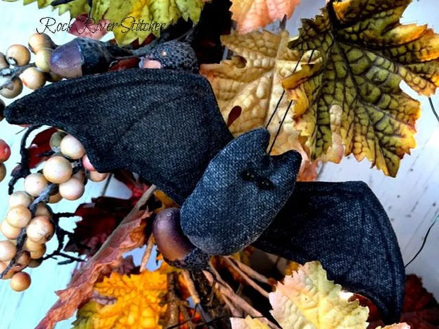 A black fabric primitive bat ornie on a fall wreath of leaves and berries