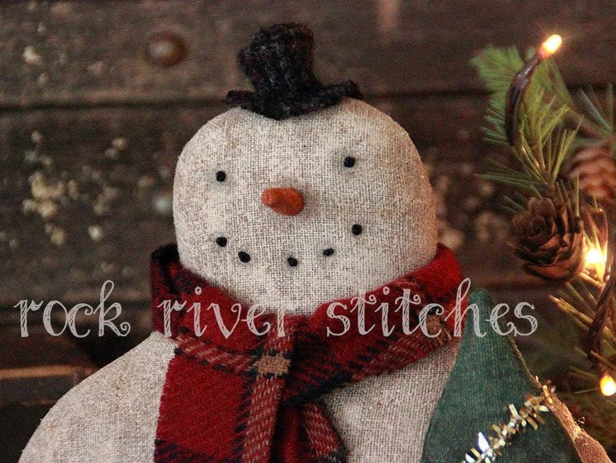 A primitive stitched snowman doll with a red plaid scarf and a black top hat