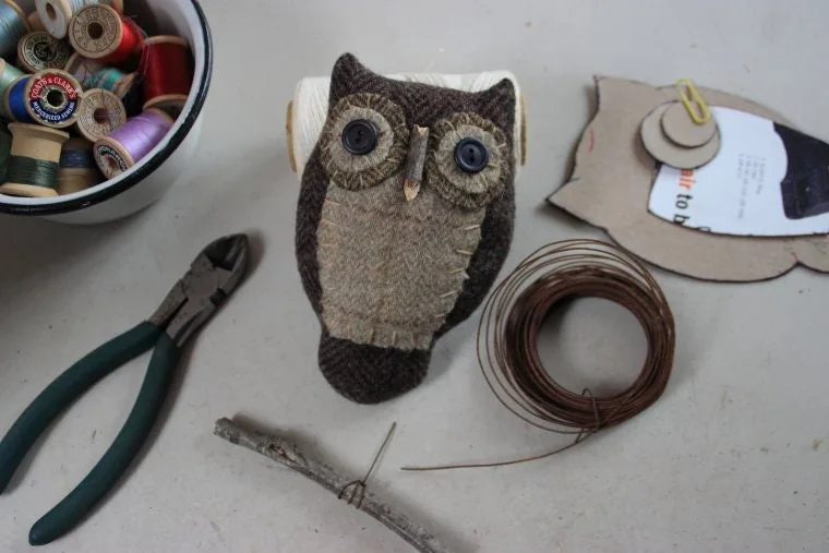 A work in progress: a stitched fabric owl on the worktable with spools of thread, pliers and a coil of wire