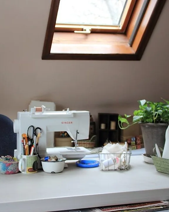 Tammy's attic workspace: a sewing machine on a white worktable under a skylight, with a potted plant and a dress form